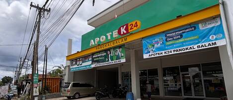 Una farmacia con fachada verde y amarilla, varios letreros y un cielo despejado.