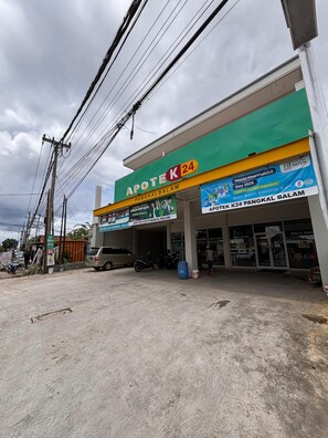 Una farmacia con fachada verde y amarilla, varios letreros y un cielo despejado.