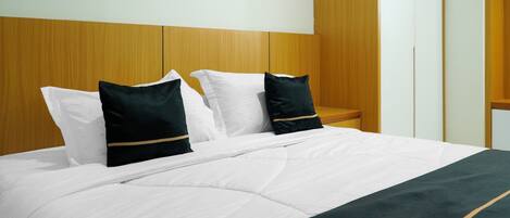 Una cama bien hecha con ropa blanca y dos almohadillas oscuras con un detalle dorado.
