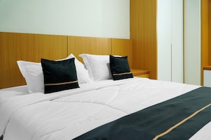 Una cama bien hecha con ropa blanca y dos almohadillas oscuras con un detalle dorado.