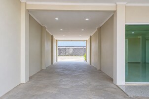Un pasillo con piso de concreto que lleva a un espacio exterior con vista a una pared de piedra y una estructura azul.