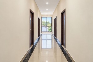 Un pasillo largo y estrecho con suelo reflectante, que conduce a un ventanal con vistas a árboles y un edificio.