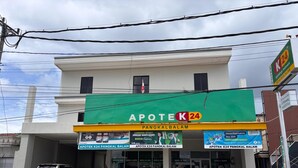 Una farmacia llamada Apotek K24 con un letrero verde, una camioneta estacionada frente y motocicletas afuera.