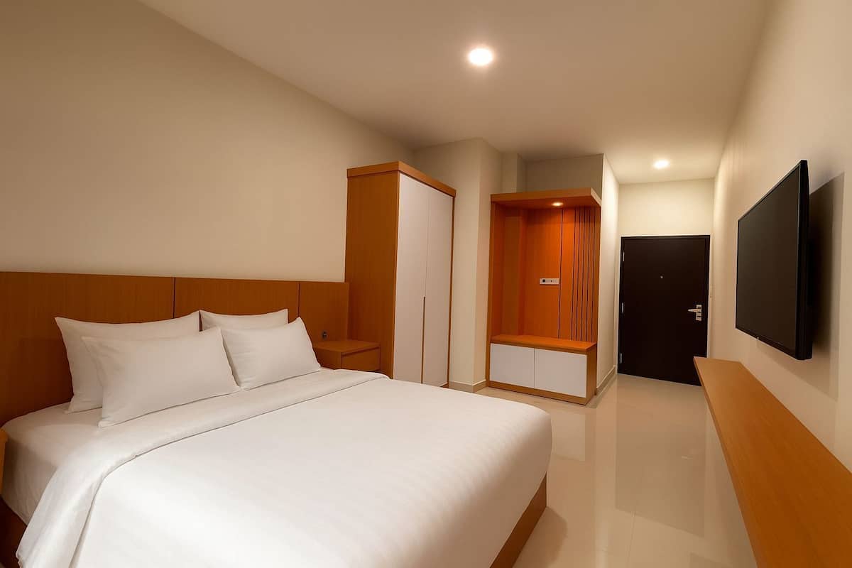 Ein Hotelzimmer mit einem großen Bett, einem Kleiderschrank, einem Fernseher und einer Tür.
