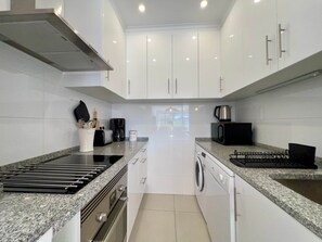 A modern kitchen with white cabinets, a built-in stove, a coffee maker, and a microwave. - "Mar à Vista" Apartment (Olhos de Água)
