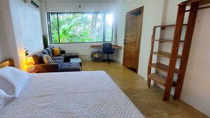 Een slaapkamer met een bed, een bureau, een stoel, een bank en een raam met uitzicht op groen.