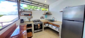 A compact kitchen with a stove, sink, and refrigerator, wooden countertops, and a window with a view.