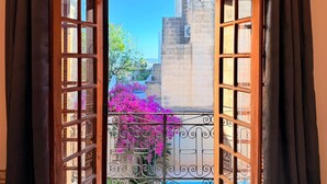 An open wooden door leading to a balcony with a wrought iron railing and pink flowers. - Charming 450-Year-Old House with Pool in Naxxar (Naxxar)