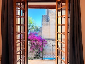 Una puerta de madera abierta que da a un balcón con barandilla de hierro forjado y flores rosas.