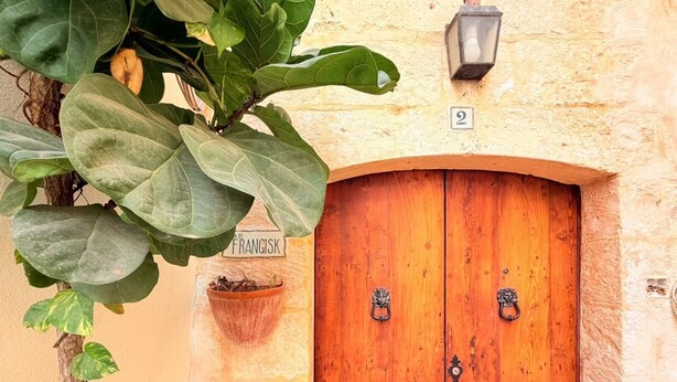 A wooden double door with a brass handle, a potted plant, and a sign above the door. - Charming 450-Year-Old House with Pool in Naxxar (Naxxar)