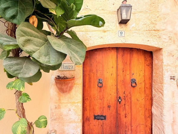 Una puerta doble de madera con un picaporte de latón, una planta en maceta y un letrero encima de la puerta.