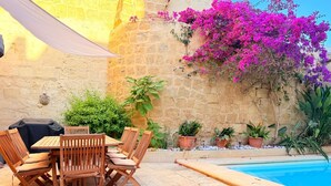 An outdoor seating area with a pool, stone walls, and potted plants. - Charming 450-Year-Old House with Pool in Naxxar (Naxxar)