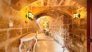 A stone-walled corridor with a white bench, a coat rack, and a staircase leading to another room. - Charming 450-Year-Old House with Pool in Naxxar (Naxxar)
