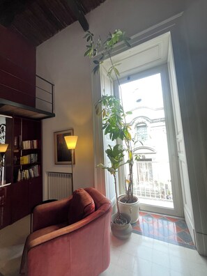 A living room with a red sofa, a bookshelf, a lamp, and a potted plant by a window. - Charming 2-beDROOMS  apartment with AC in Napoli center in spanish quarter (Napoli)