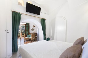 A bedroom with a bed, green curtains, a TV, and a view of an outdoor patio. - Alcova Apartment – Terrace with a View of Positano (Positano)