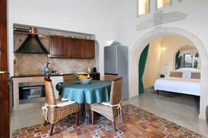 A compact kitchen with a dining area, a washing machine, and a bed in the adjacent room. - Alcova Apartment – Terrace with a View of Positano (Positano)