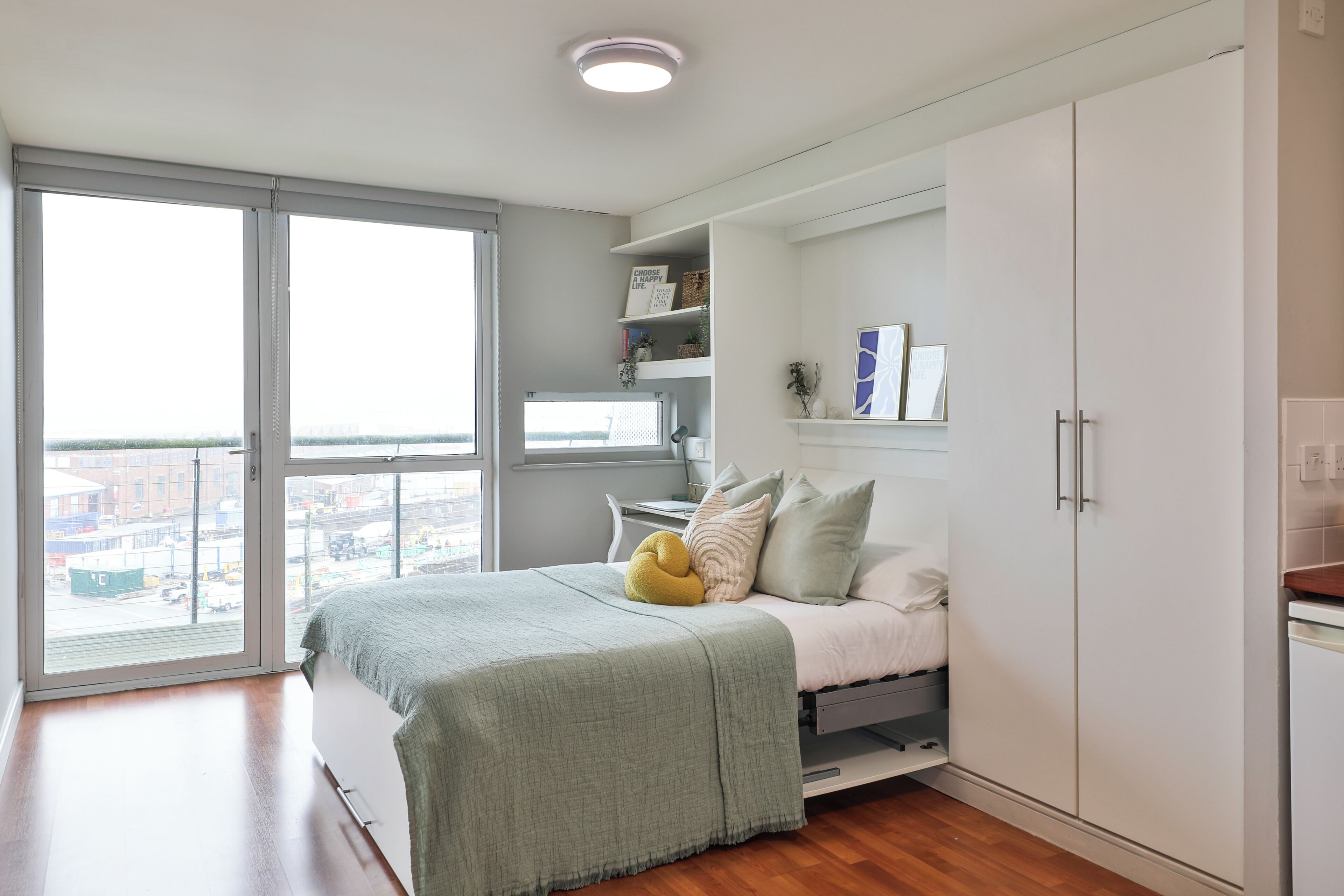 A bedroom with a bed, a wardrobe, a window, and a view of the city.