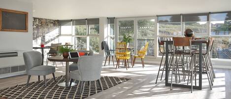 A spacious living area with large windows, a dining table, and multiple chairs.