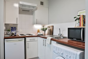 A kitchen with white cabinets, a dishwasher, a microwave, and a washing machine. - Student Only Maritime Studios (Falmouth)