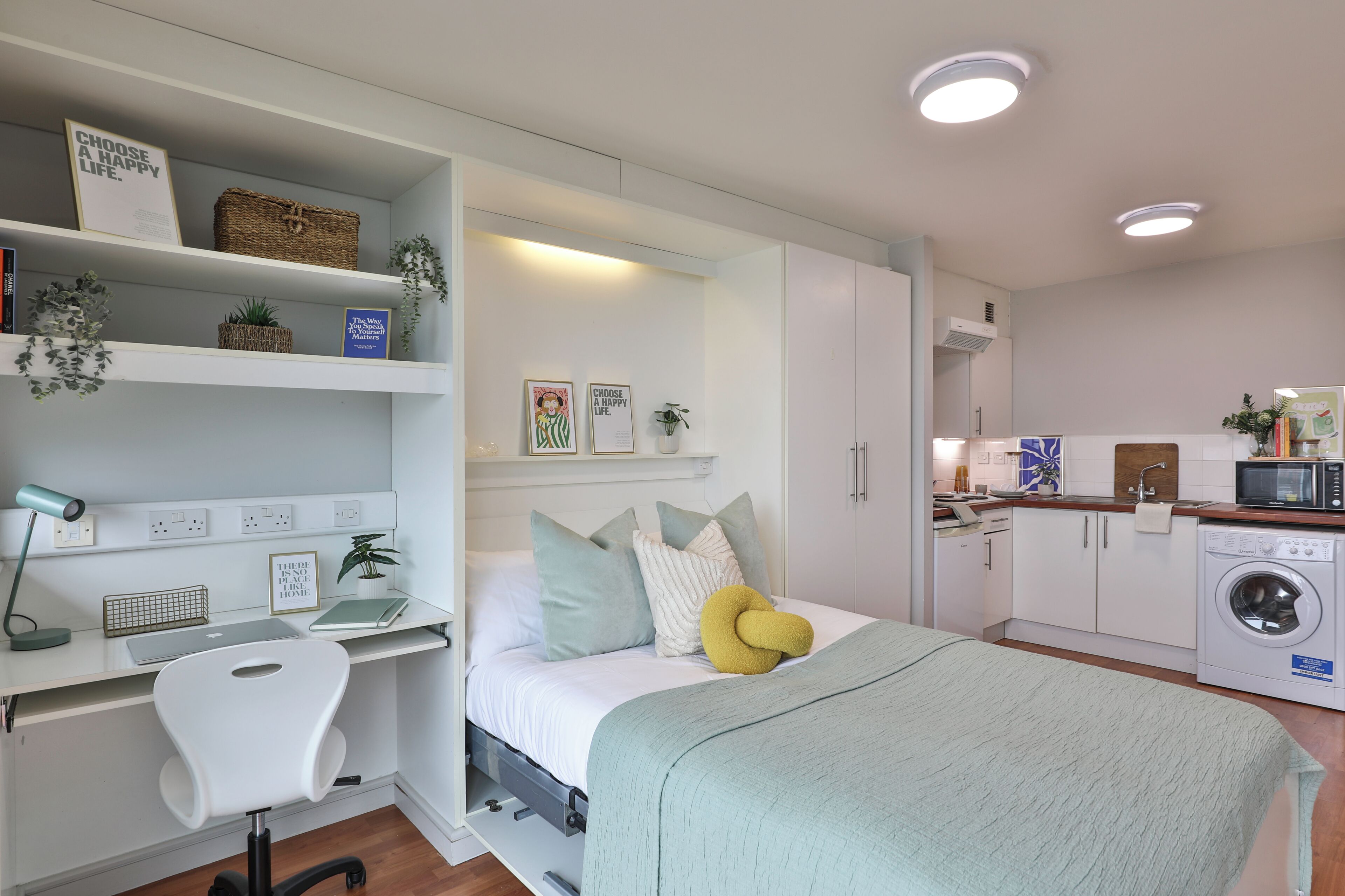 Quarto compacto com cama, mesa de cabeceira e escrivaninha com cadeira.