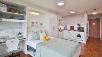 Quarto compacto com cama, mesa de cabeceira, cadeira e armário embutido.