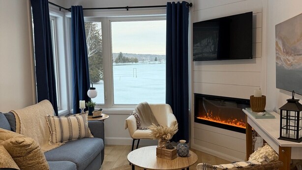 Un salon comprenant un canapé, des fauteuils, une cheminée, un téléviseur et une vue sur un lac.