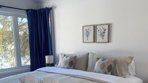 Une chambre avec un grand lit, une fenêtre avec des rideaux, une table de chevet et deux tableaux accrochés au mur.