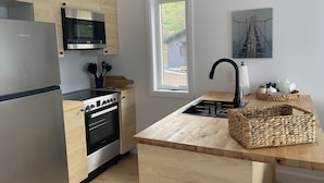 Une cuisine moderne avec des meubles en bois, des appareils électroménagers en acier inoxydable, une fenêtre et une vue sur une maison à l’extérieur.