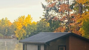 Une cabane au bord d’un lac, avec un quai, entourée du feuillage automnal.