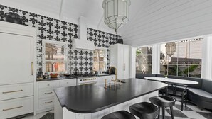 A kitchen with a central island, bar stools, a window with blinds, and a patterned backsplash. - Wedged Inn (Dunmore Town)