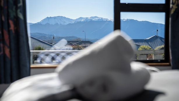 Un lit avec un oreiller, une fenêtre donnant sur des montagnes enneigées et un lampadaire à l’extérieur.