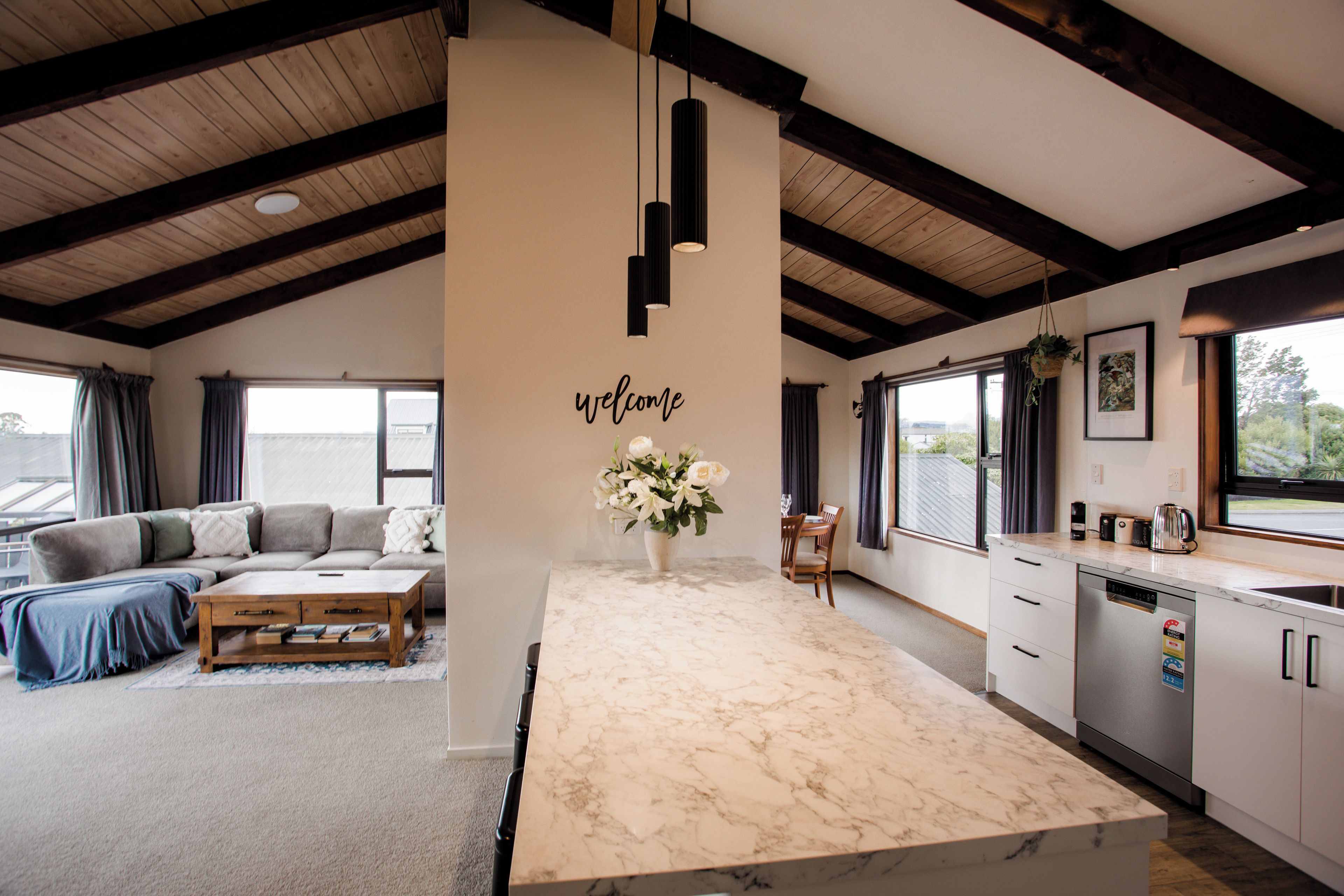 A modern kitchen with a marble countertop, a dining area with a sofa, and a living room with a large window.