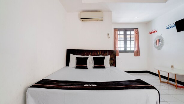 Een hotelkamer met een bed, een tafeltje, een airconditioner, een raam met gordijnen en een aan de muur bevestigde televisie.