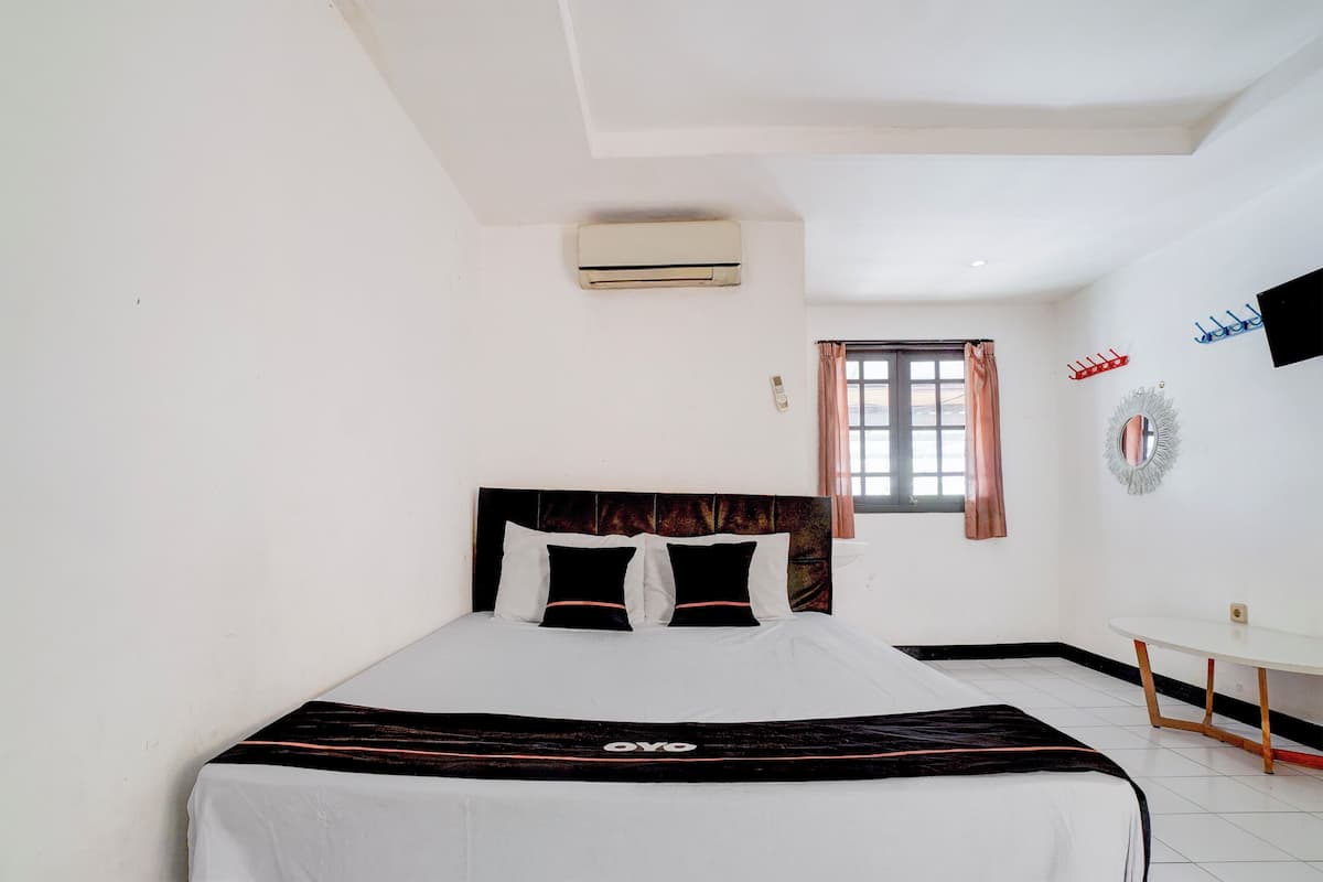 A hotel room with a bed, a small table, an air conditioner, a window with curtains, and a wall-mounted TV.