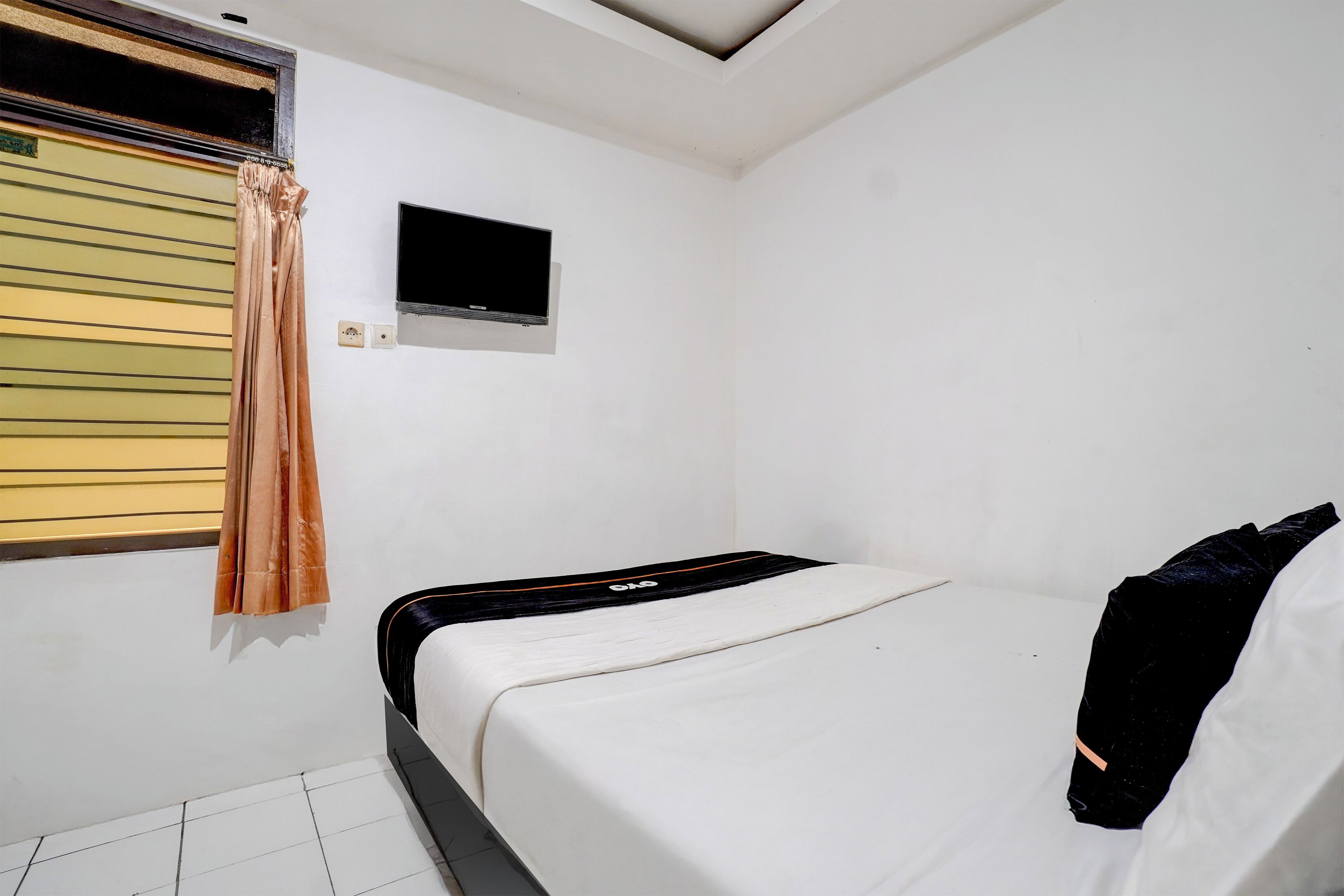 A bedroom with a bed, a television mounted on the wall, and a window with blinds.