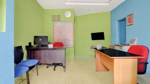 Een kamer met een bureau, stoelen, een kaart, een klok en een ingelijst certificaat aan de muur.