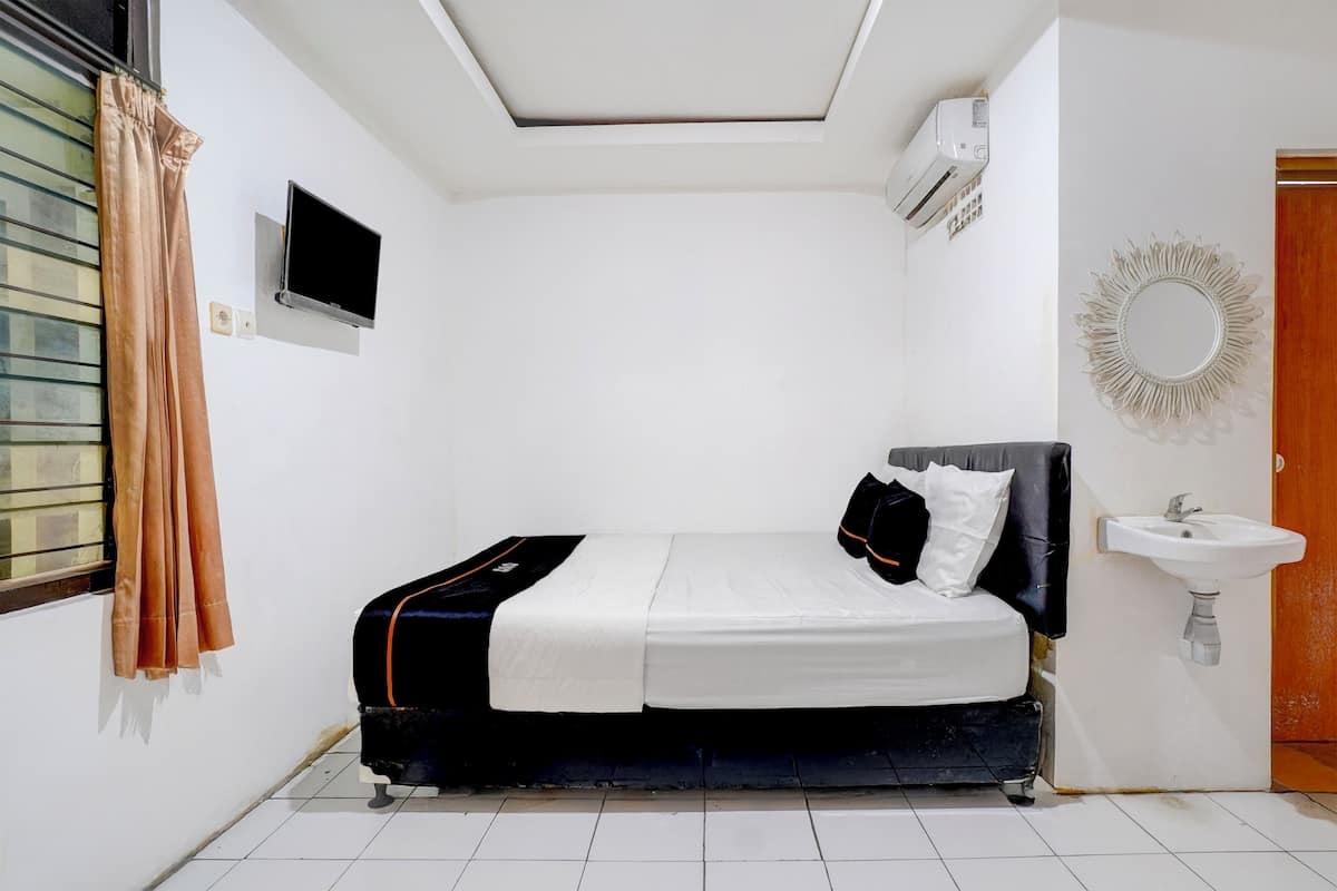 A bedroom with a bed, a TV, an air conditioner, a window with curtains, and a sink.