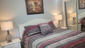 Ein ordentlich bezogenes Bett mit Streifenmuster, zwei Nachttische mit Lampen, ein Spiegel und ein gerahmtes Bild an der Wand.