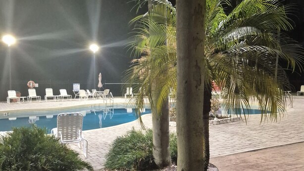 Ein Poolbereich bei Nacht mit Liegestühlen und Palmen.