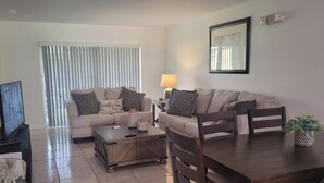 Ein Wohnzimmer mit Sofa, Couchtisch, Fernseher und Esstisch.