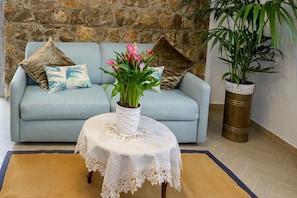A light blue sofa with patterned cushions, a small round table with a lace tablecloth, and a potted plant. - Aury House – Sea and Nature in Ieranto (Massalubrense)