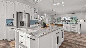 Une cuisine moderne avec des meubles blancs, un grand îlot central, des appareils en acier inoxydable et des luminaires suspendus.