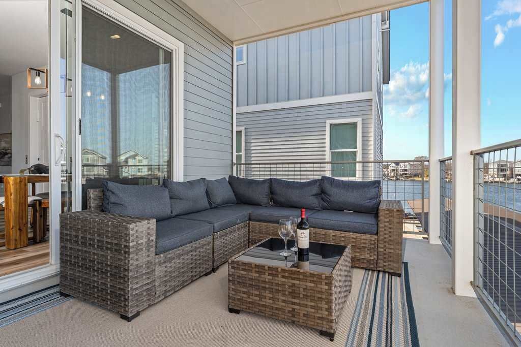 A balcony with a wicker sofa, a glass coffee table, and a bottle of wine.