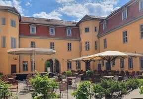 Un patio con asientos al aire libre, un escenario y un edificio con varias ventanas y puertas.