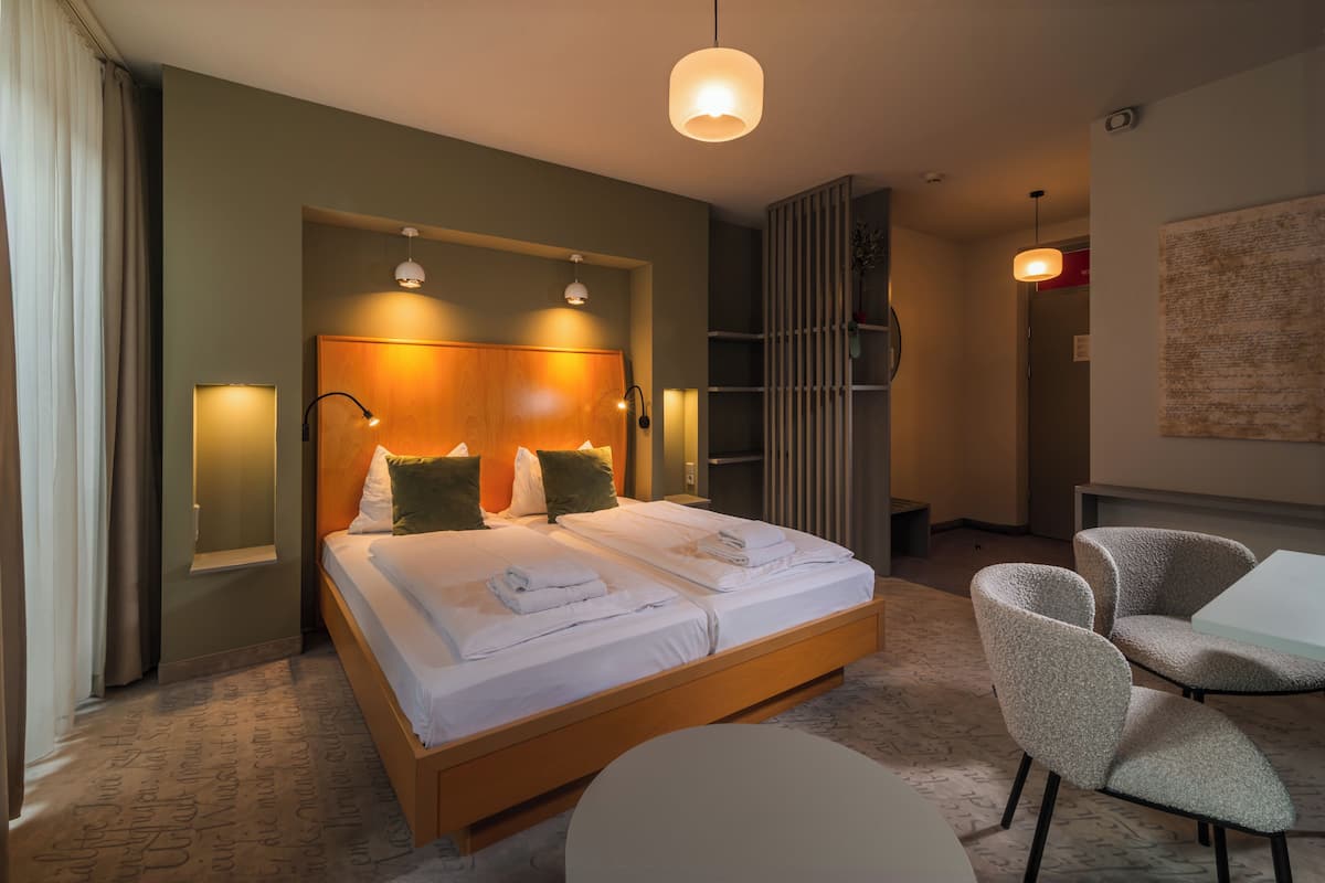 Una habitación de hotel con una cama grande, lámparas de noche, un área de estar con sillas y una mesita.