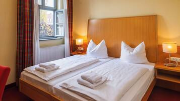 Habitación de hotel con una cama grande, dos mesitas de noche con lámparas, una ventana con cortinas y una alfombra roja.