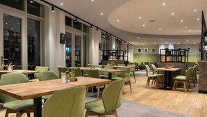 A modern restaurant with green upholstered chairs, wooden tables, and a circular ceiling design. - Erbenhof (Weimar)