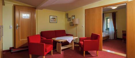 Una habitación con un sofá rojo, una mesita con mantel de encaje, una lámpara de pie y una puerta de madera.