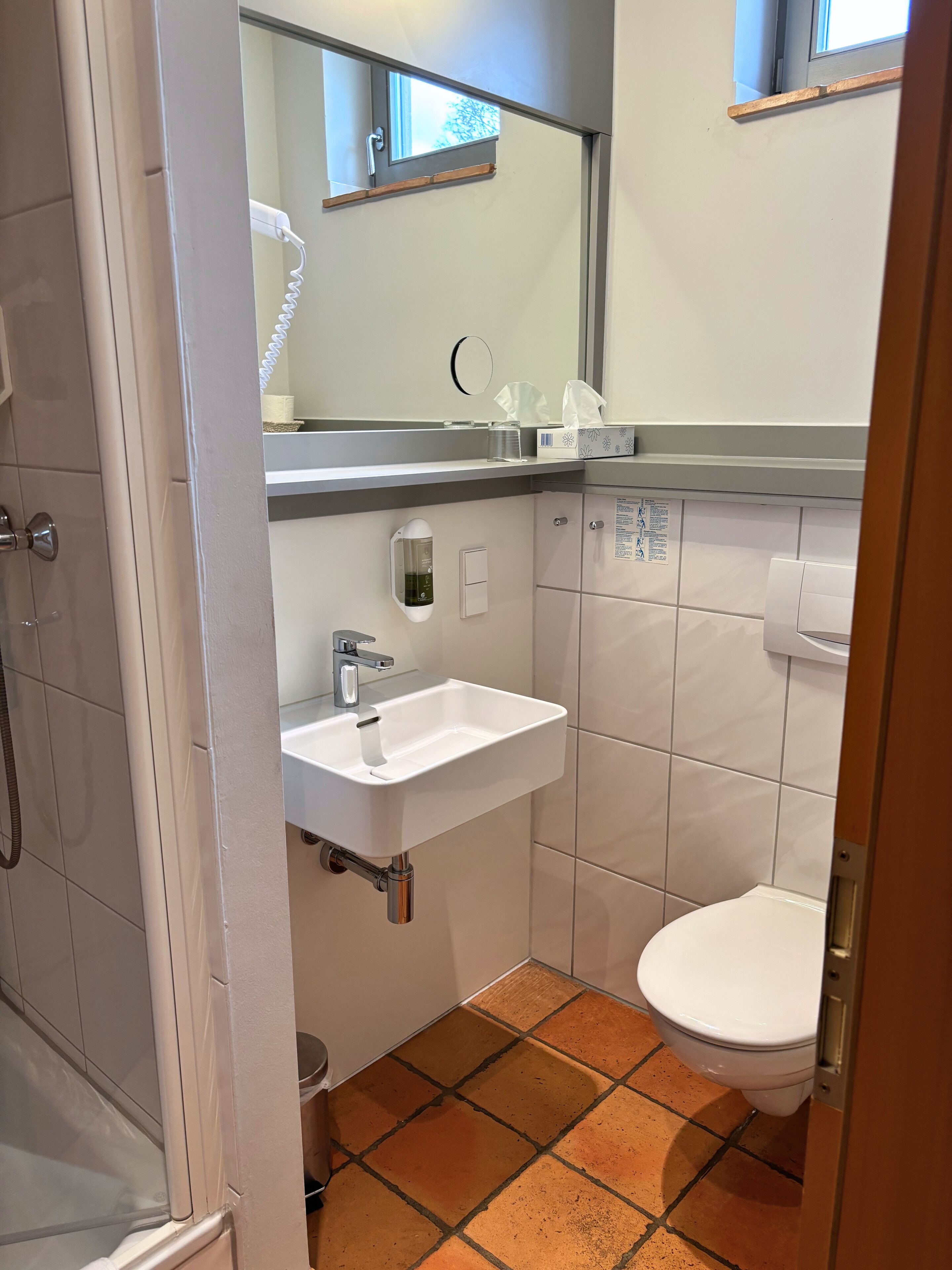 Ein Badezimmer mit weißem Waschbecken, einem Spiegel, einer Toilette und einer Duschkabine.