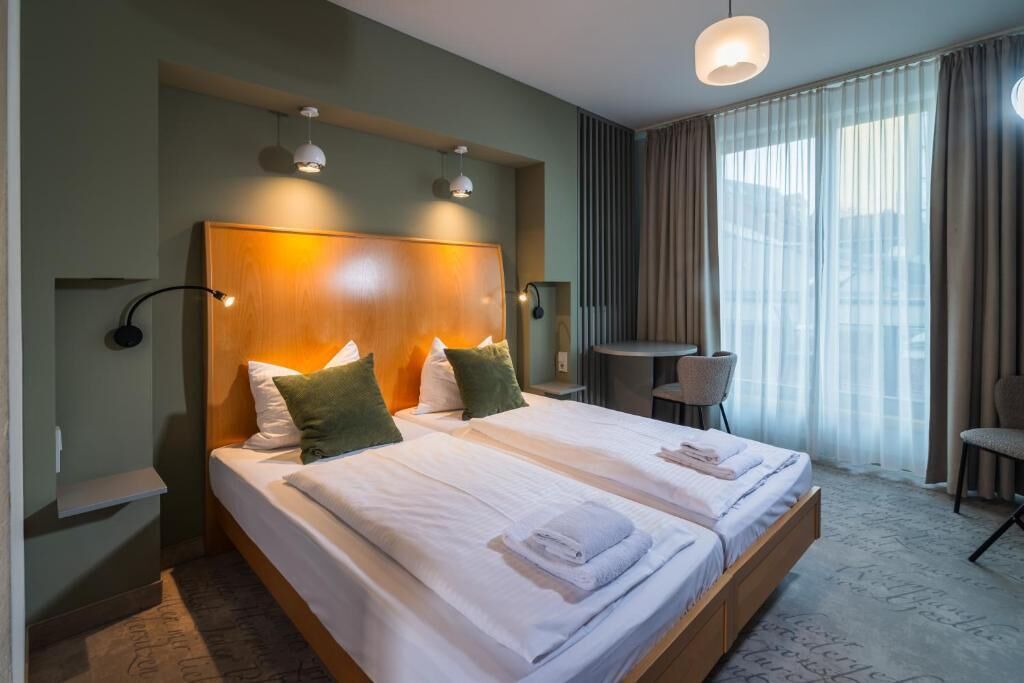 Une chambre d’hôtel avec deux lits, un bureau, une chaise et une grande fenêtre avec des rideaux.